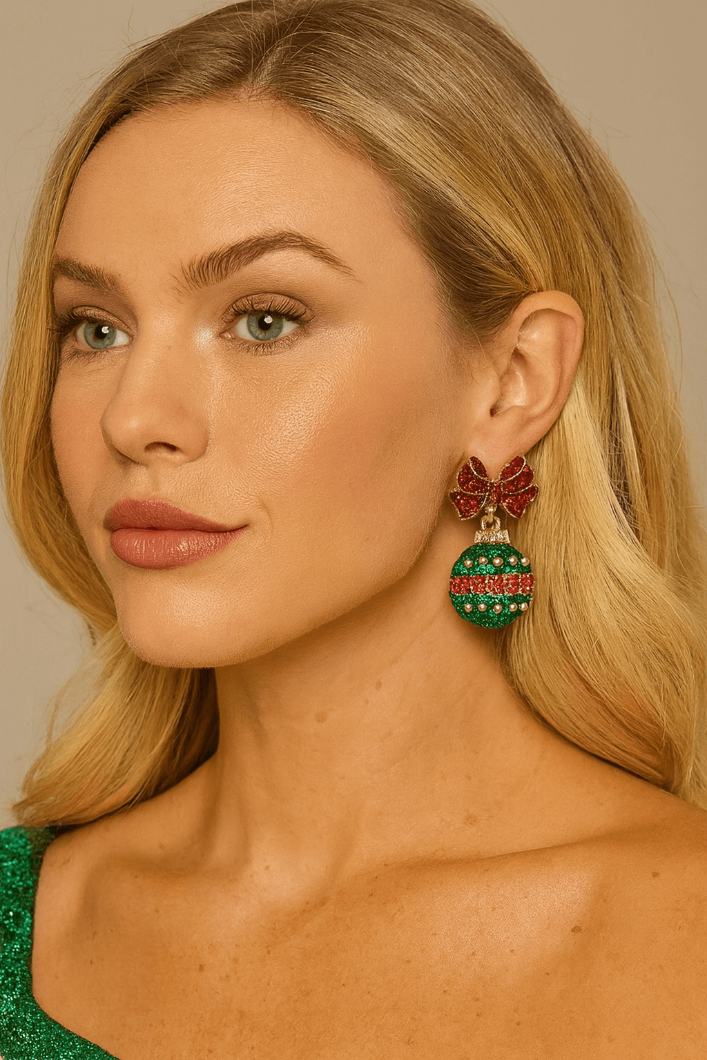 Woman wearing festive rhinestone ornament earrings featuring a red glitter bow and a green-and-red jeweled ornament charm.