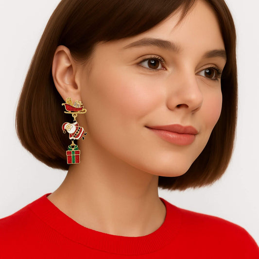 Woman wearing festive holiday dangle earrings with a glittery red sleigh, Santa charm, and green-and-red gift box.