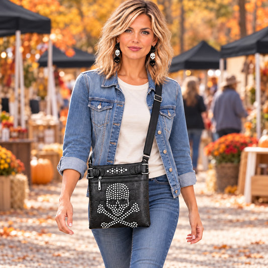 Black rhinestone skull crossbody bag with an embossed skull pattern, worn with denim at an outdoor fall market.